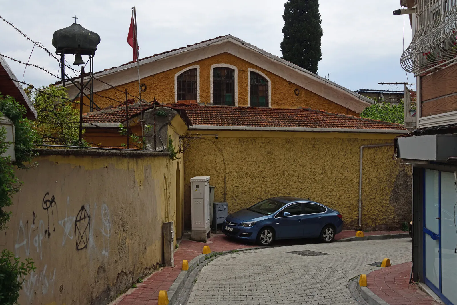 Ο ναός και το καμπαναριό του πάνω από τον ψηλό μαντρότοιχο της αυλής, από τον δρόμο