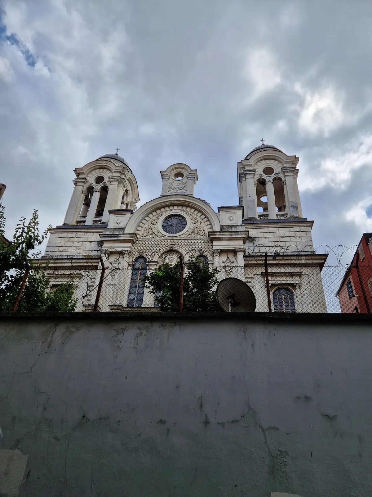 Η δυτική πρόσοψη και τα δύο καμπαναριά της Παναγίας Ελπίδας πάνω από τον τοίχο της αυλής